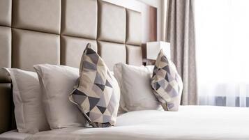 A hotel room with a large padded headboard, a bed with white bedding, and decorative pillows.