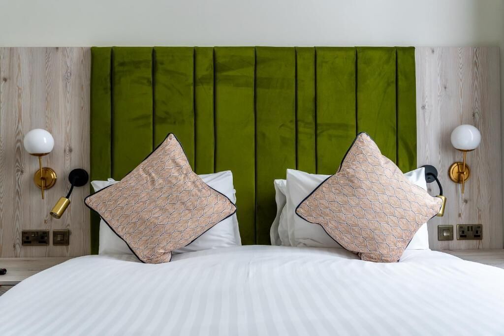 Un letto con lenzuola bianche, una testiera imbottita in verde e cuscini decorati.