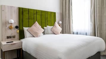 A hotel room with a large bed, a green headboard, two bedside tables with lamps, and a window with curtains.