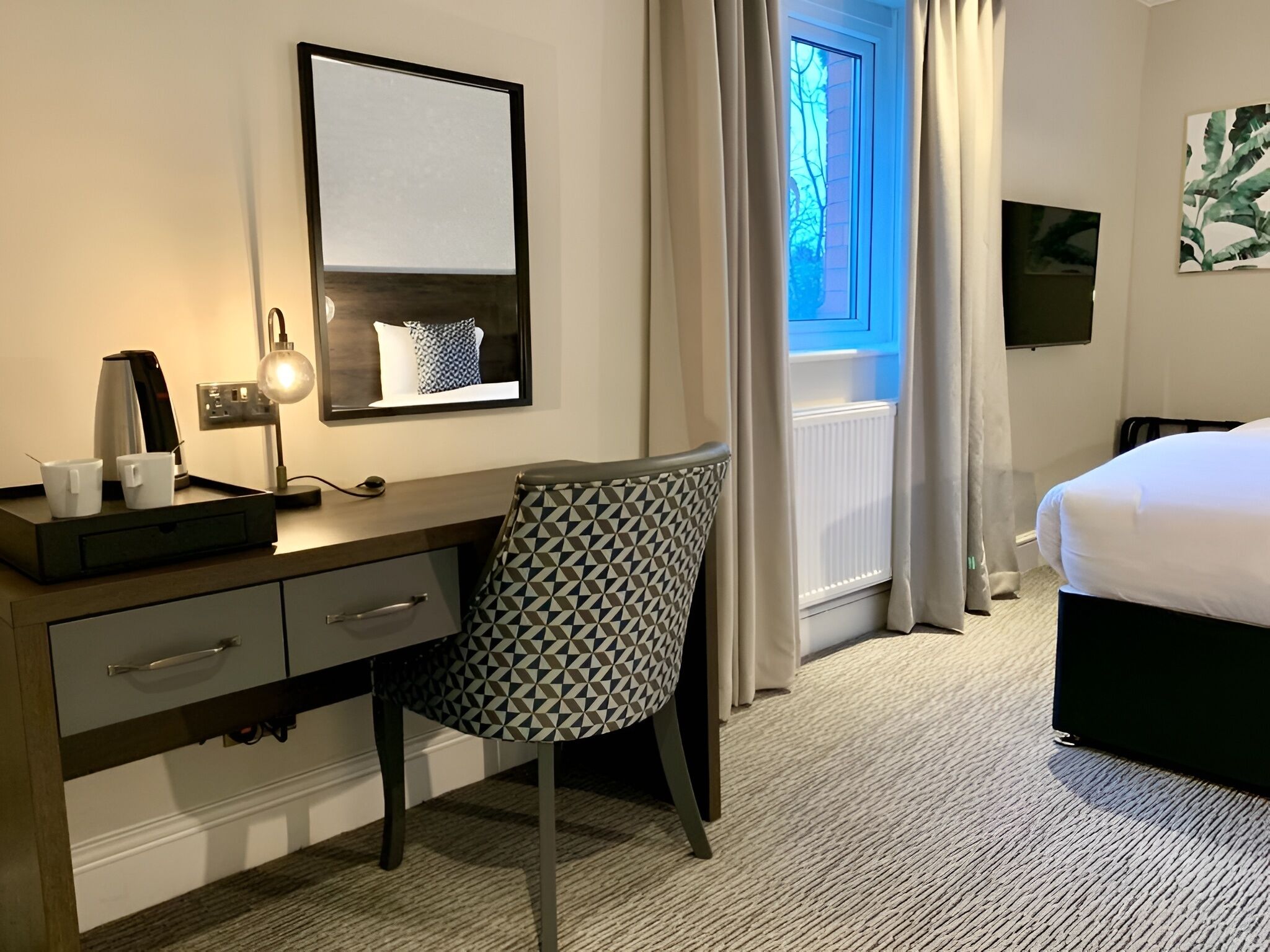 Ein Hotelzimmer mit Schreibtisch, Stuhl, Bett und einem Fenster mit Vorhängen.