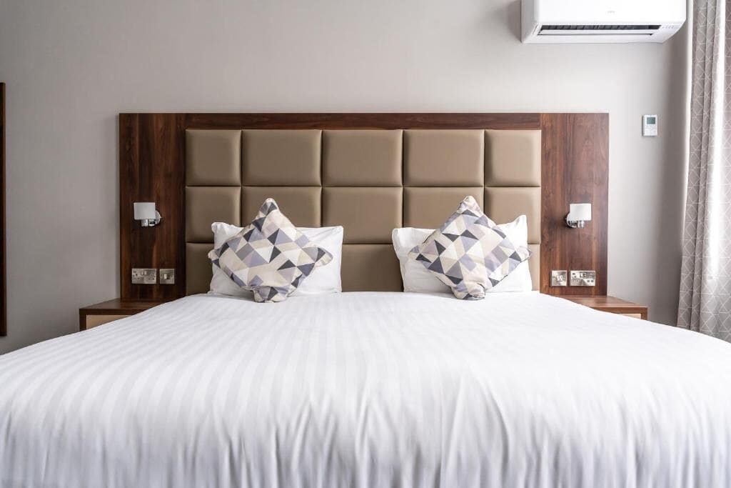 A hotel room with a large bed, two nightstands, a wooden headboard, and an air conditioning unit.