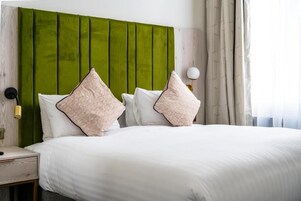 Una cama con ropa de cama blanca, cabecera verde y almohadas estampadas.