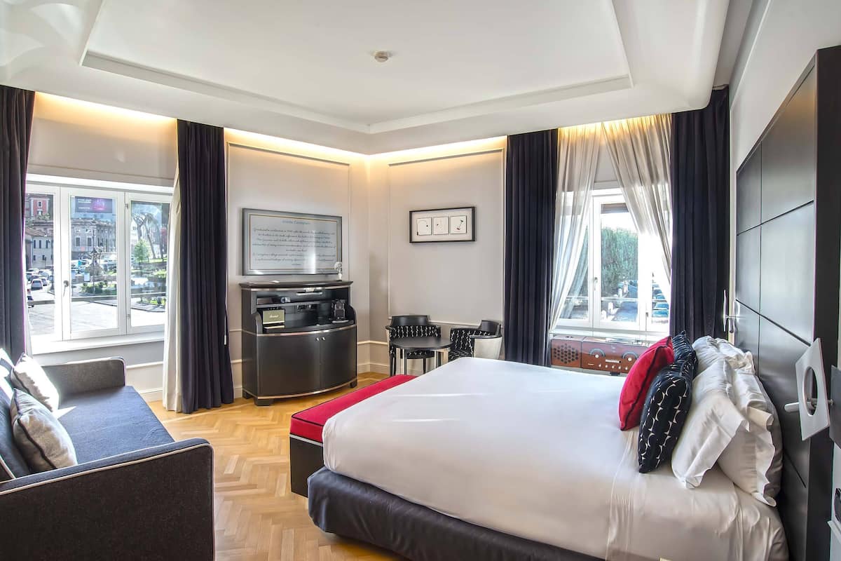 A hotel room with a bed, a desk, a TV, and a view of the city.