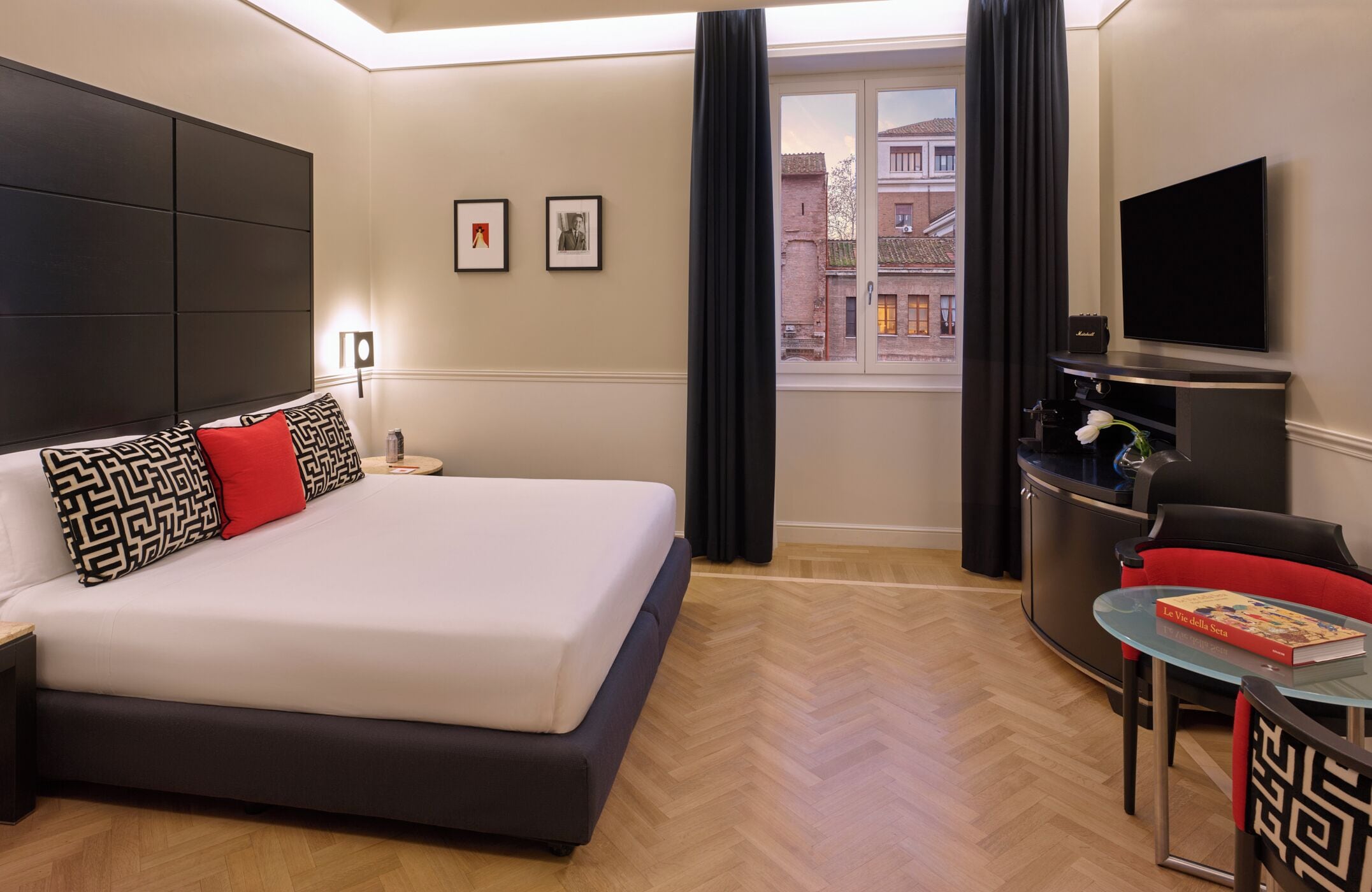 Moderni hotellihuone, jossa on suuri sänky, työpöytä tuolilla, taulutelevisio ja taideteoksia seinällä.