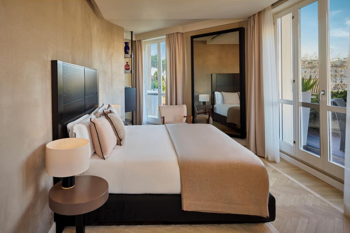 Une chambre d’hôtel moderne avec un grand lit, une table de chevet avec une lampe, un grand miroir et une vue sur l’extérieur.