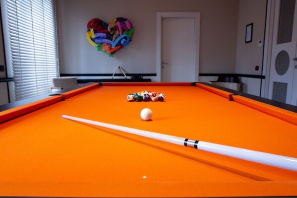 Ein Billardtisch mit Kugeln und Spielstange, eine herzförmige Dekoration an der Wand und eine Tür im Hintergrund.