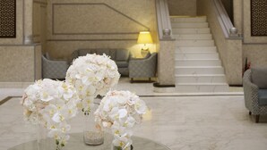 A lobby with a grand chandelier, a staircase, and a round glass table with white flowers. - Carlton Tower Hotel (Dubai)