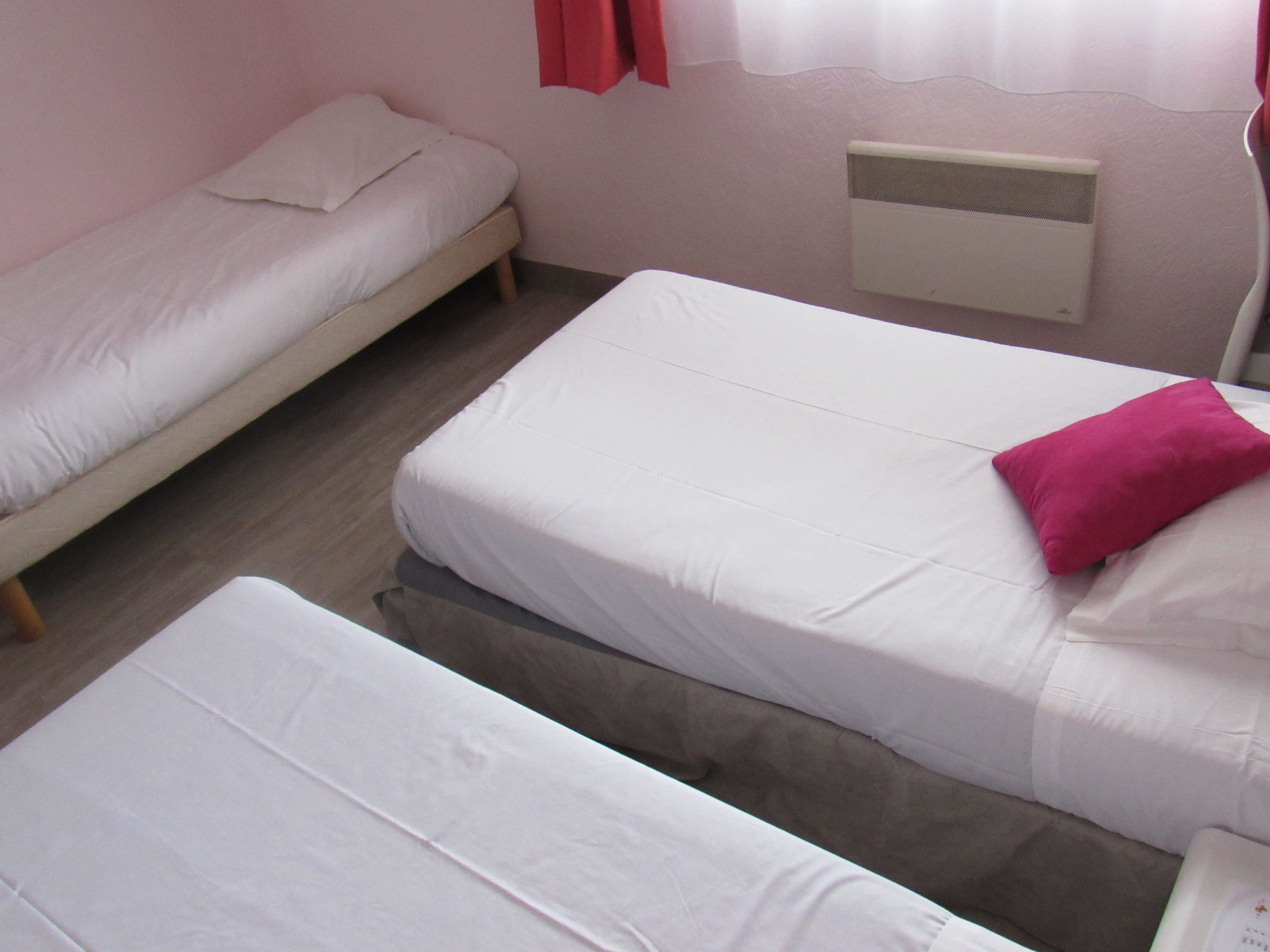 A room with two single beds, one with a pink pillow, and a small heater on the wall.