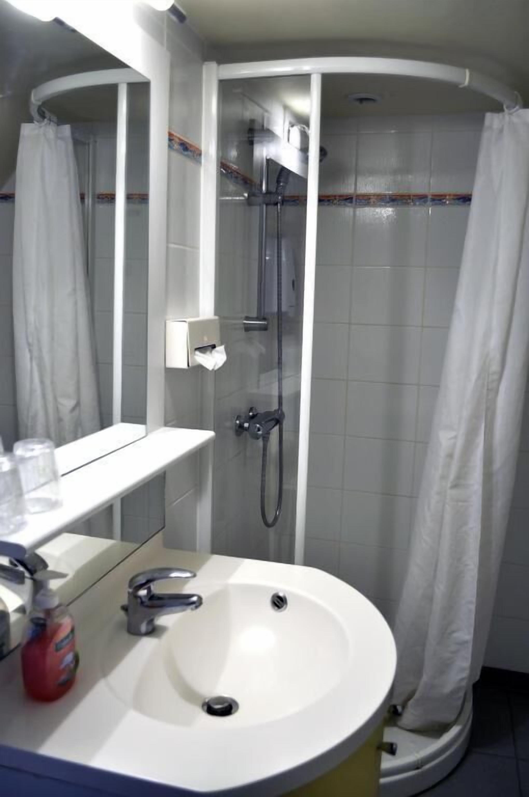 A bathroom with a white sink, a mirror, a shower, and a towel rack.