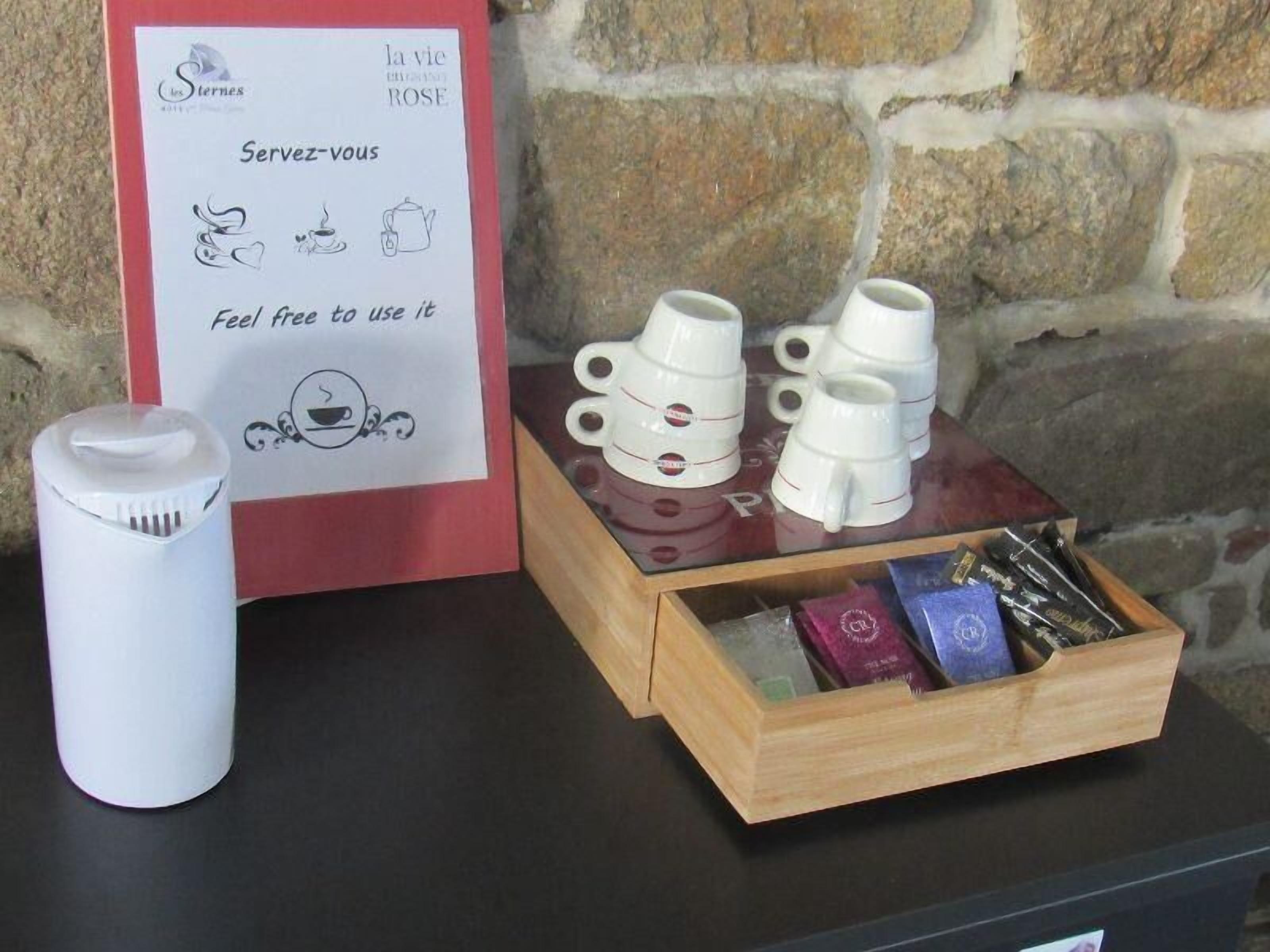 Uma mesa com uma placa, um recipiente branco e uma caixa de madeira com chávenas e saquetas de chá.