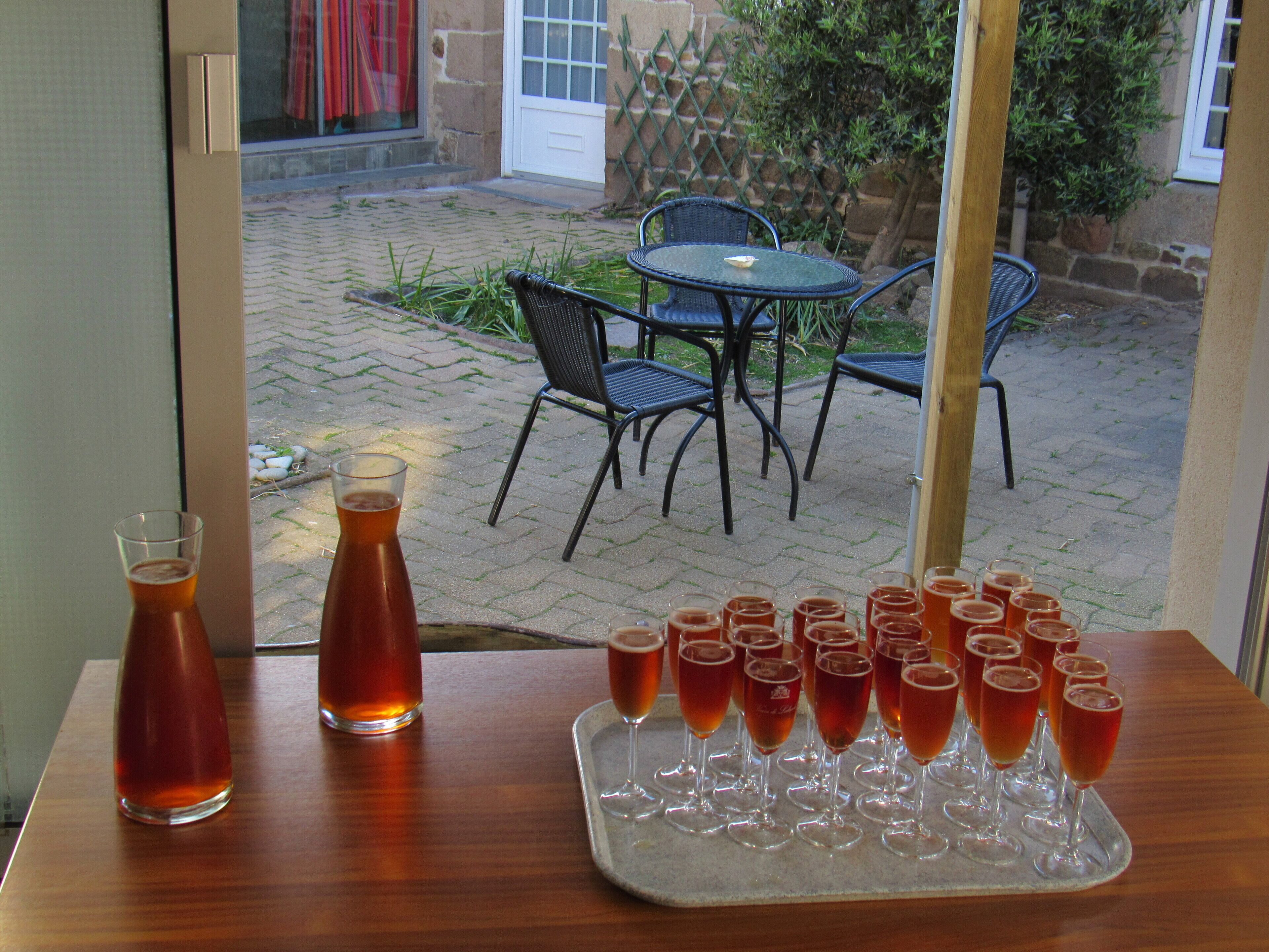 A table with a pitcher and glasses of a beverage, a window with a view of a patio area with chairs and a table.