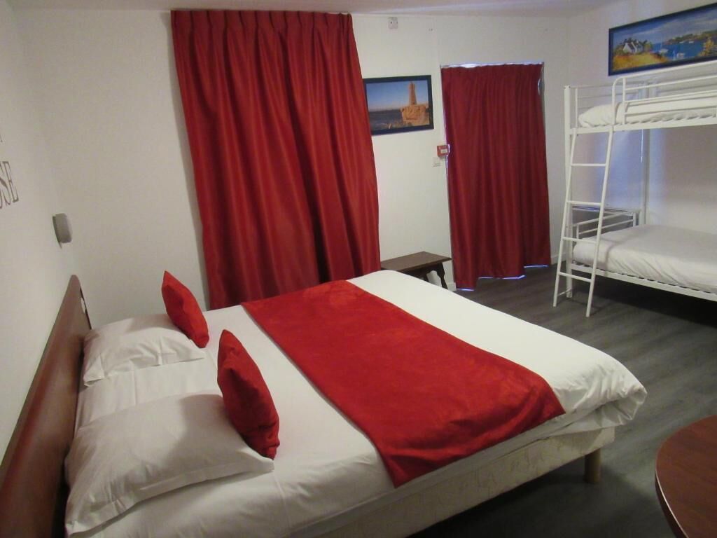 Une chambre avec un lit simple, un lit superposé, une petite table et des rideaux rouges.
