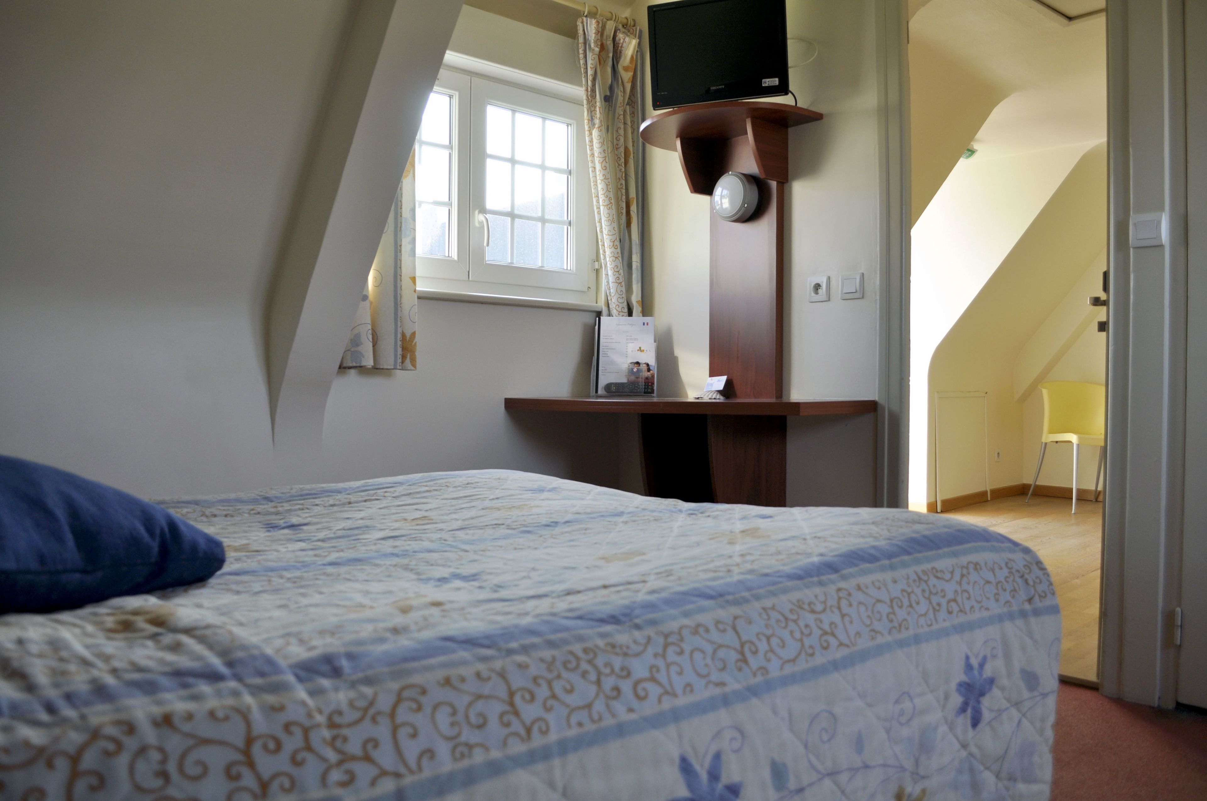 Un dormitorio con cama, escritorio con computadora, ventana con cortinas y vista a otra habitación.