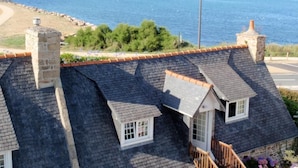 A coastal property with multiple gabled roofs, a stone chimney, and a view of the sea and beach. - Hôtel Les Sternes  (Louannec)
