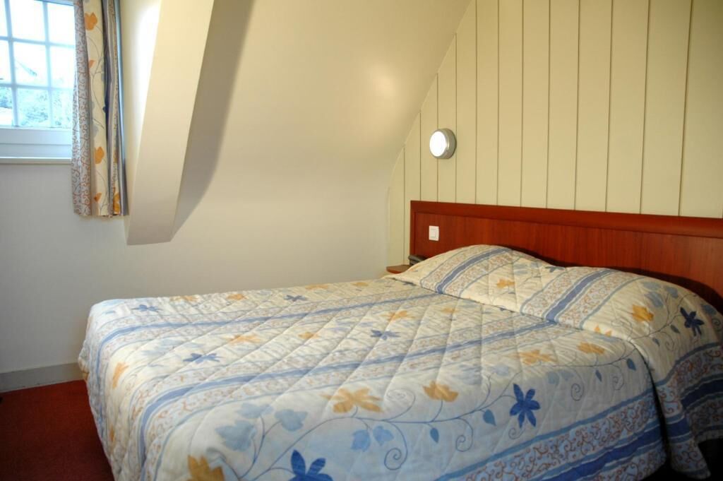 Une chambre à coucher avec un lit, une fenêtre avec des rideaux et un luminaire fixé au mur.