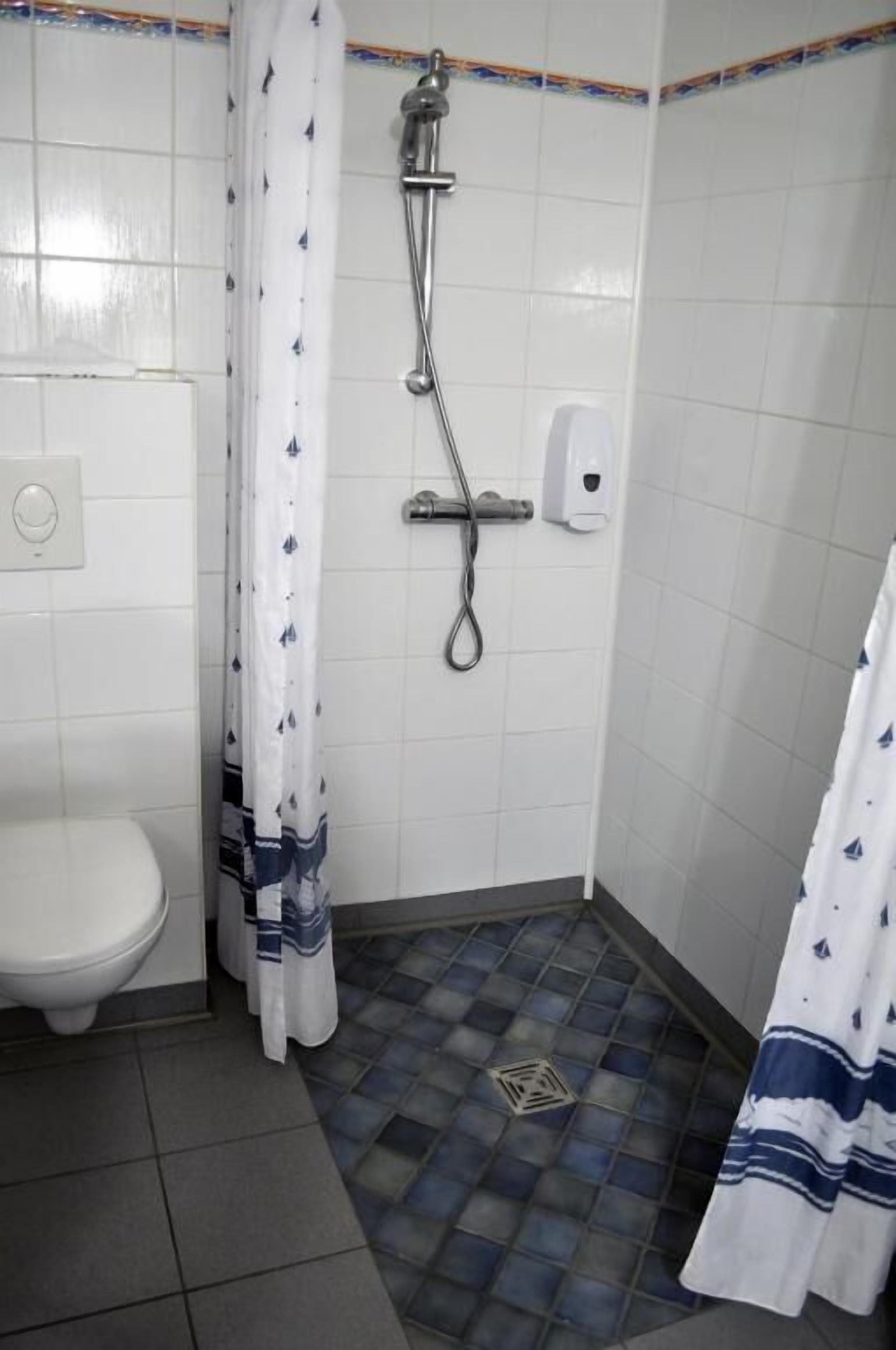 A small bathroom with a white toilet, a shower with a curtain, and a soap dispenser on the wall.