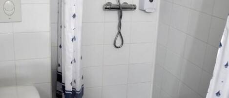 Un baño pequeño con un inodoro blanco, una ducha con cortina y un dispensador de jabón en la pared.