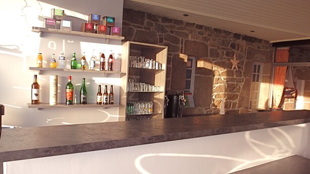 A bar area with shelves stocked with bottles and glasses, a stone wall, and a star decoration. - Hôtel Les Sternes  (Louannec)