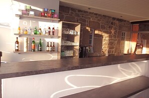 A bar area with shelves stocked with bottles and glasses, a stone wall, and a star decoration. - Hôtel Les Sternes  (Louannec)