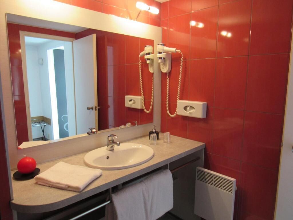 Un baño con lavamanos, espejo, azulejos rojos y secador de pelo.