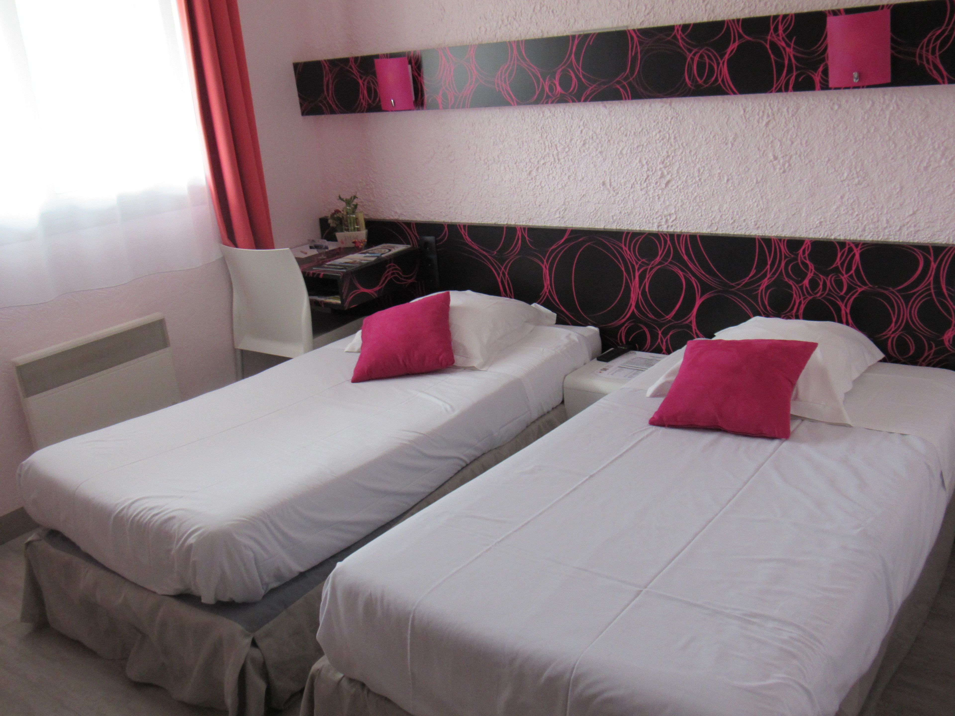 Habitación de hotel con dos camas individuales, un escritorio y una silla.