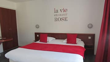 A neatly made bed with a red blanket and pillows, a wooden headboard, and a wall with the text "la vie en GRANIT ROSE".