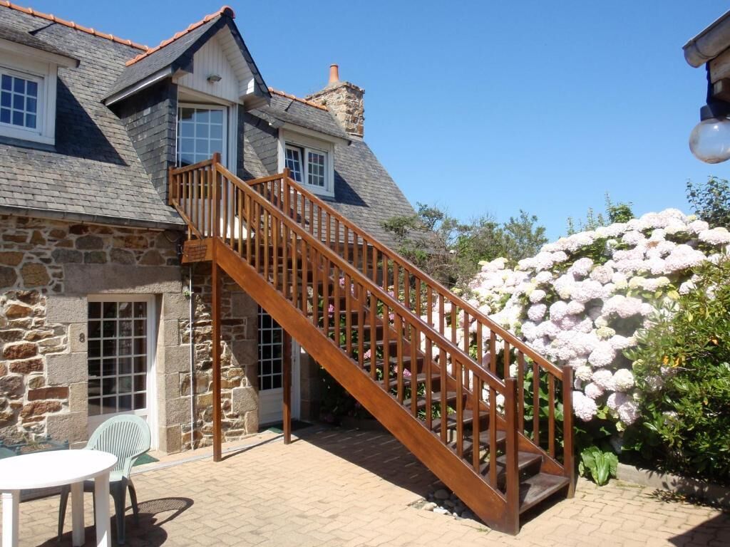 A stone house with a wooden staircase leading to a balcony.