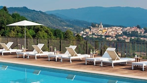 Zona junto a la piscina con sillas de descanso y vistas a un pueblo al fondo.