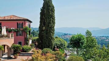 A pink villa with a courtyard, a tall cypress tree, and a view of distant mountains.