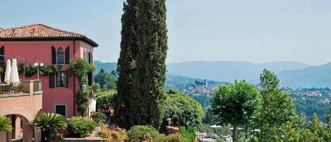 A pink villa with a courtyard, a tall cypress tree, and a view of distant mountains.
