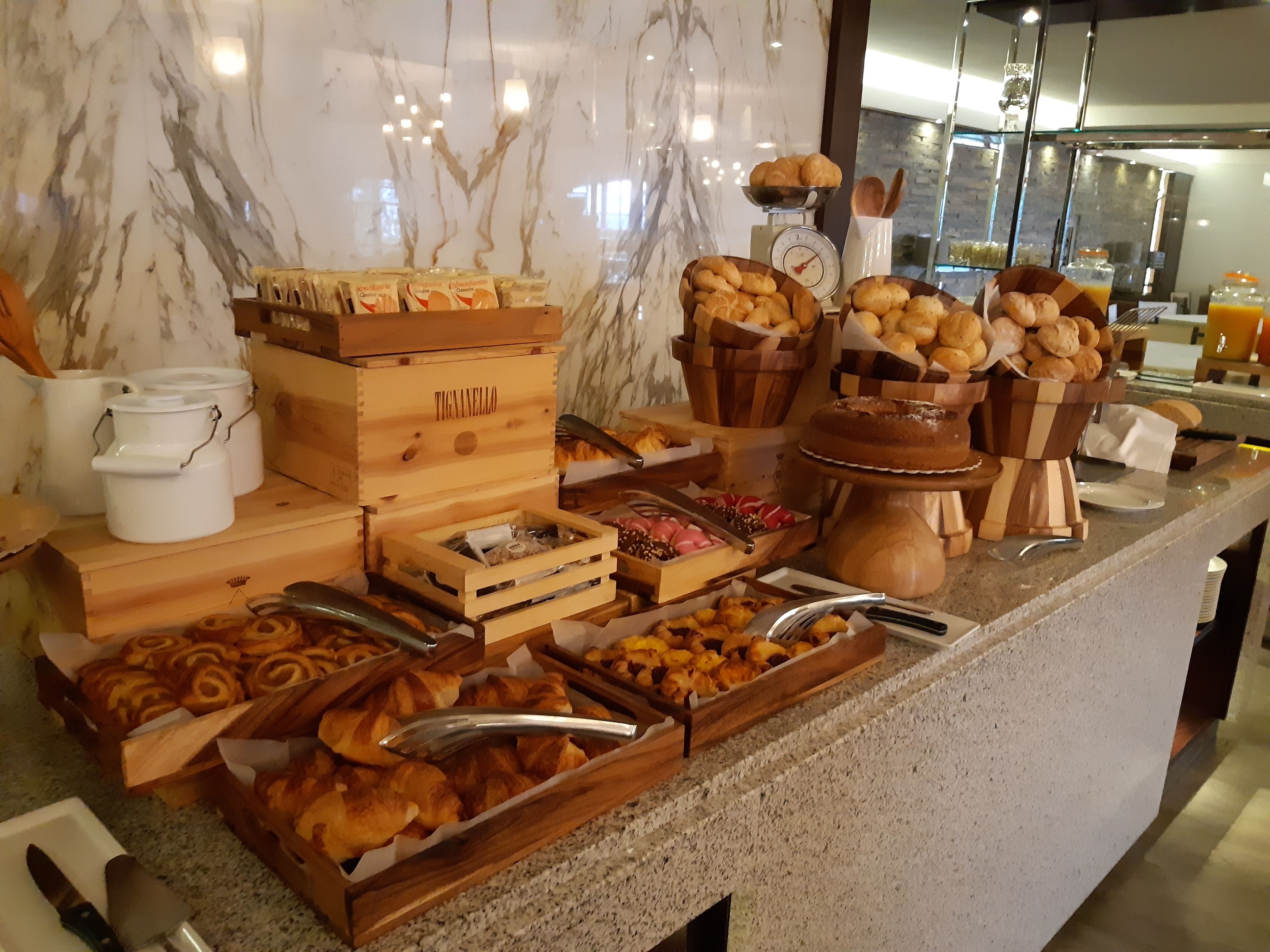 A buffet with various baked goods, including pastries and bread, arranged on a marble countertop.