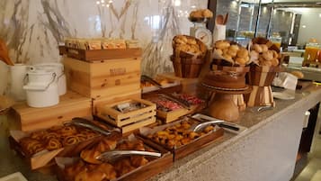 A buffet with various baked goods, including pastries and bread, arranged on a marble countertop.