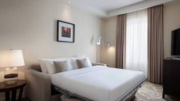 Ein Hotelzimmer mit Bett, Schreibtisch, Lampe, Fernseher und einem Bild an der Wand.