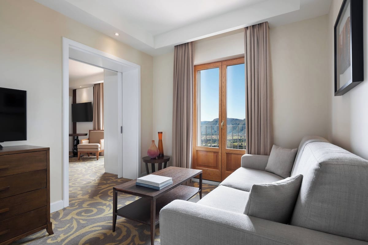 A hotel room with a sofa, a television, a desk, and a view of the outdoors.