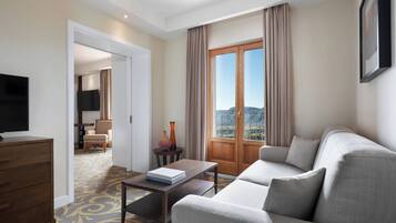 Ein Hotelzimmer mit einer Couch, einem Fernseher, einem Schreibtisch und Blick ins Freie.