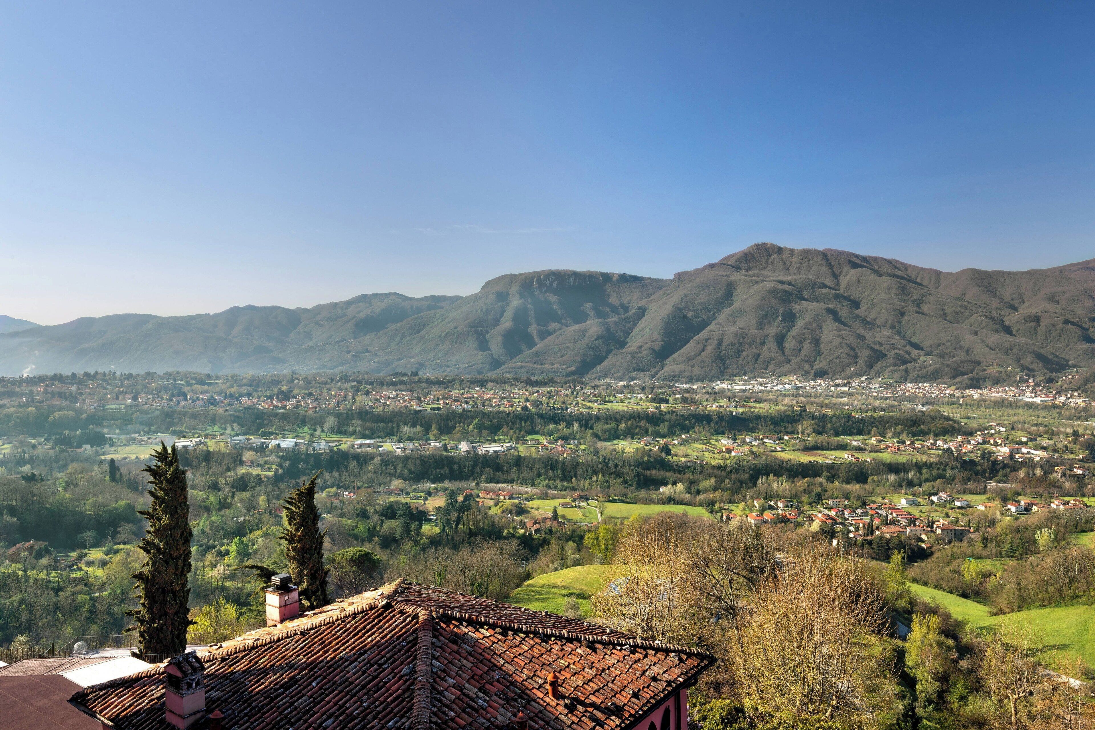 A view of a town with a prominent mountain in the background, a clear sky, and a building with a tiled roof in the foreground.
