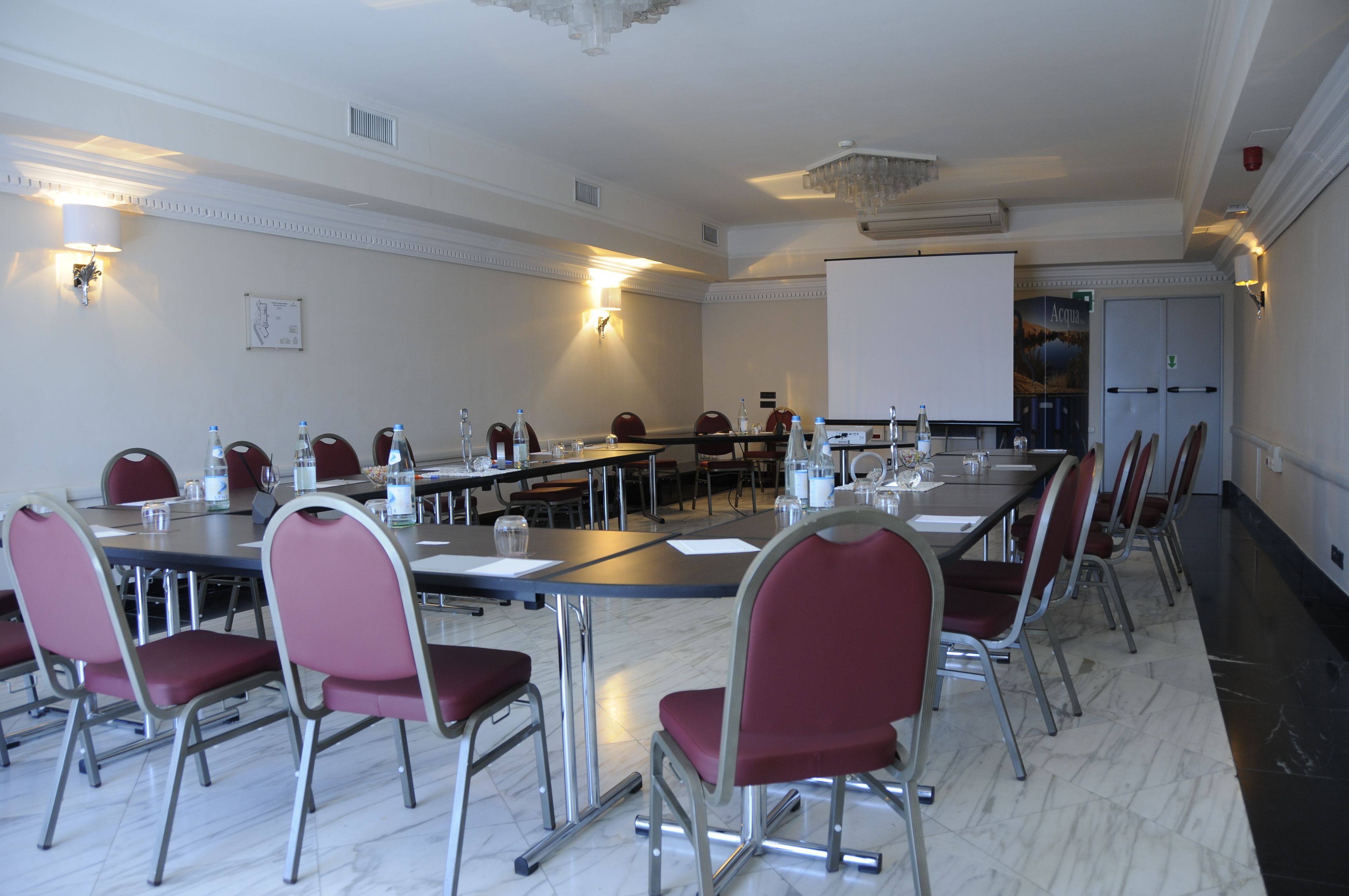 Ein Konferenzraum mit langem Tisch, roten Stühlen und einer Projektionsleinwand.