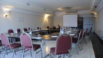 Ein Konferenzraum mit langem Tisch, roten Stühlen und einer Projektionsleinwand.