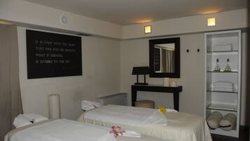 Habitación de hotel con dos camas, un espejo grande, un estante con toallas y una frase motivadora en la pared.