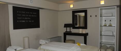 Habitación de hotel con dos camas, un espejo grande, un estante con toallas y una frase motivadora en la pared.