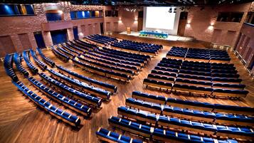 Ein großer Saal mit Reihen blauer Sitze und einer Bühne im Vordergrund.