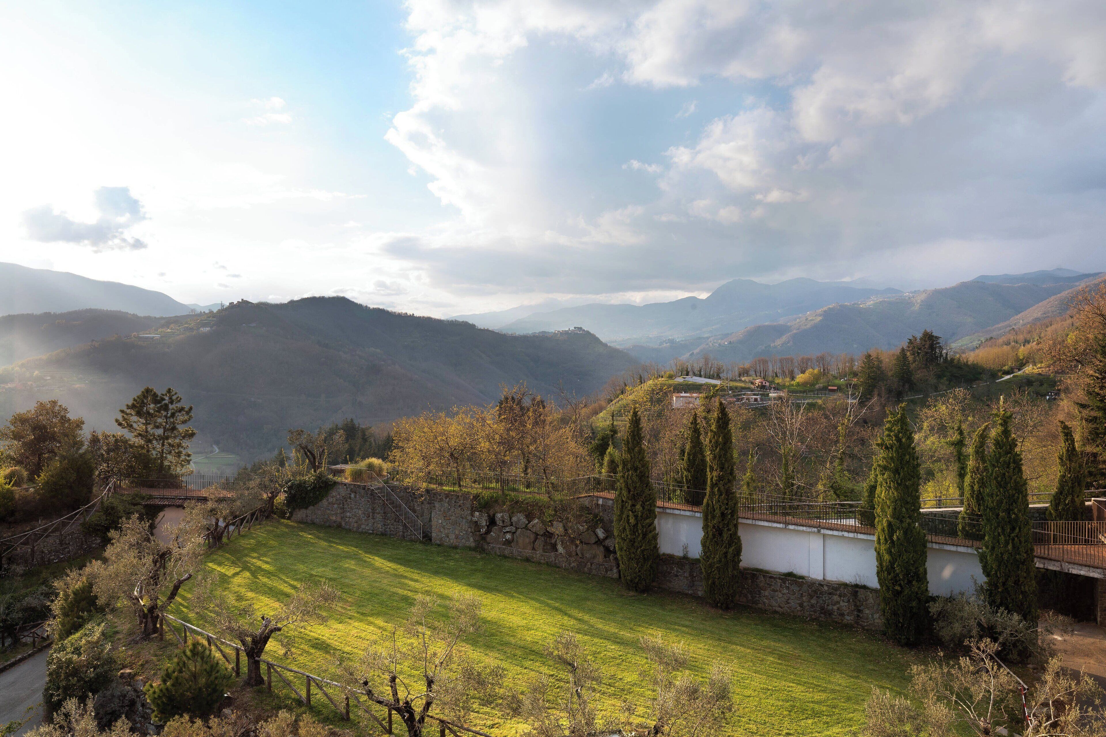 Ländliche Landschaft mit Steinmauer, Wiesen und Bergen in der Ferne.