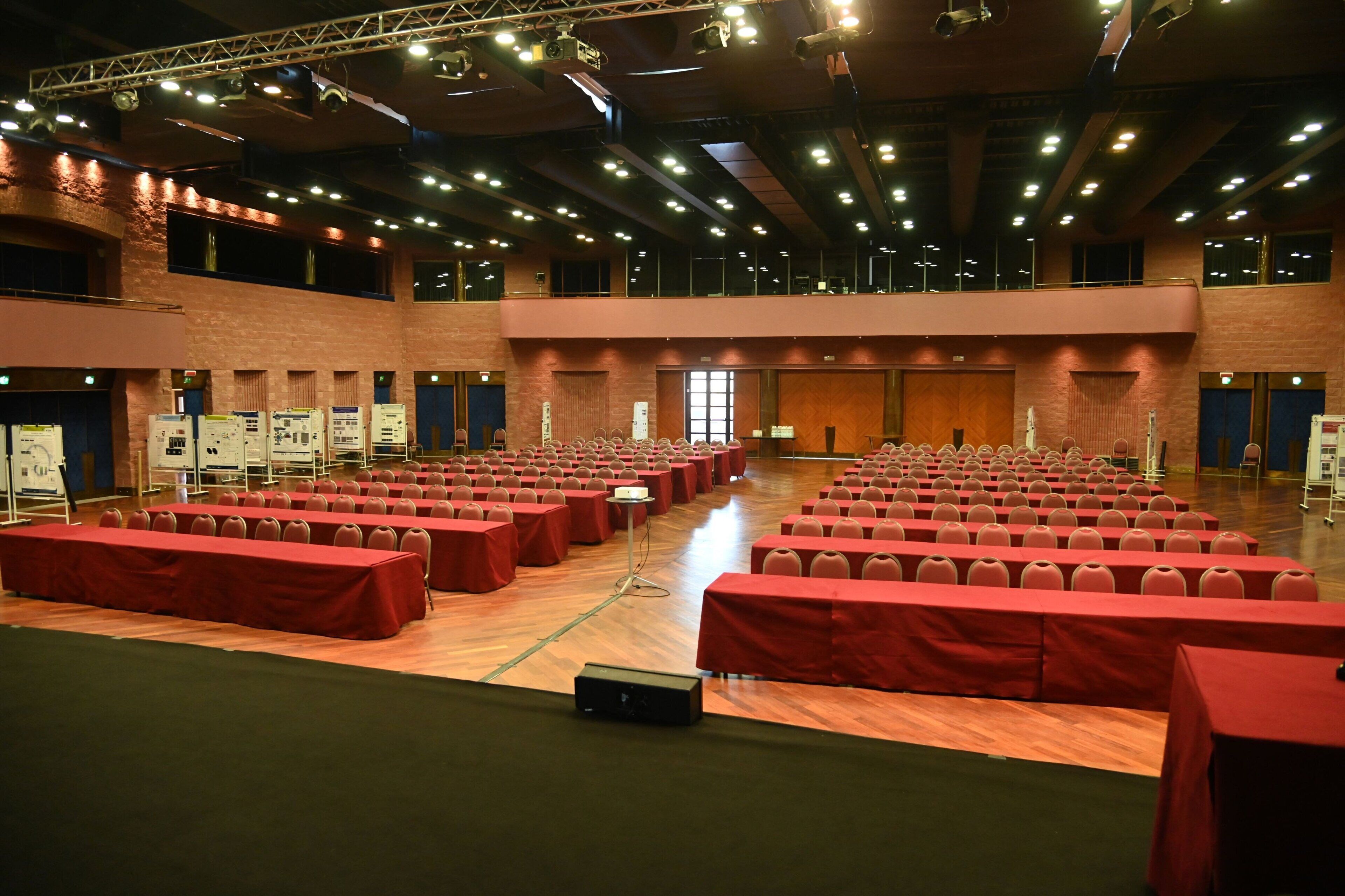 A large hall with rows of tables and chairs, a stage, and a balcony.