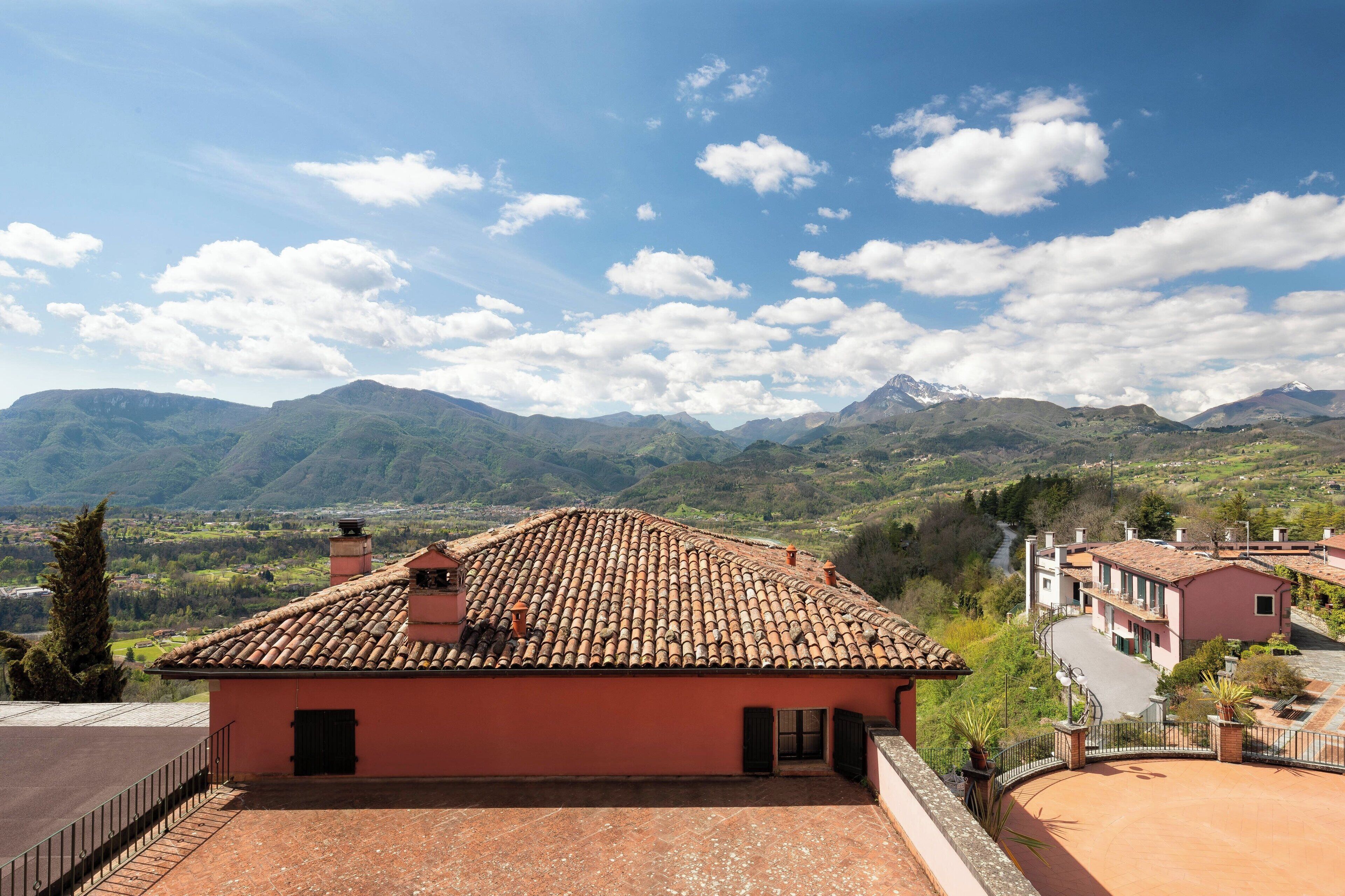 A terracotta-roofed building with a courtyard, surrounded by mountains and a clear sky.