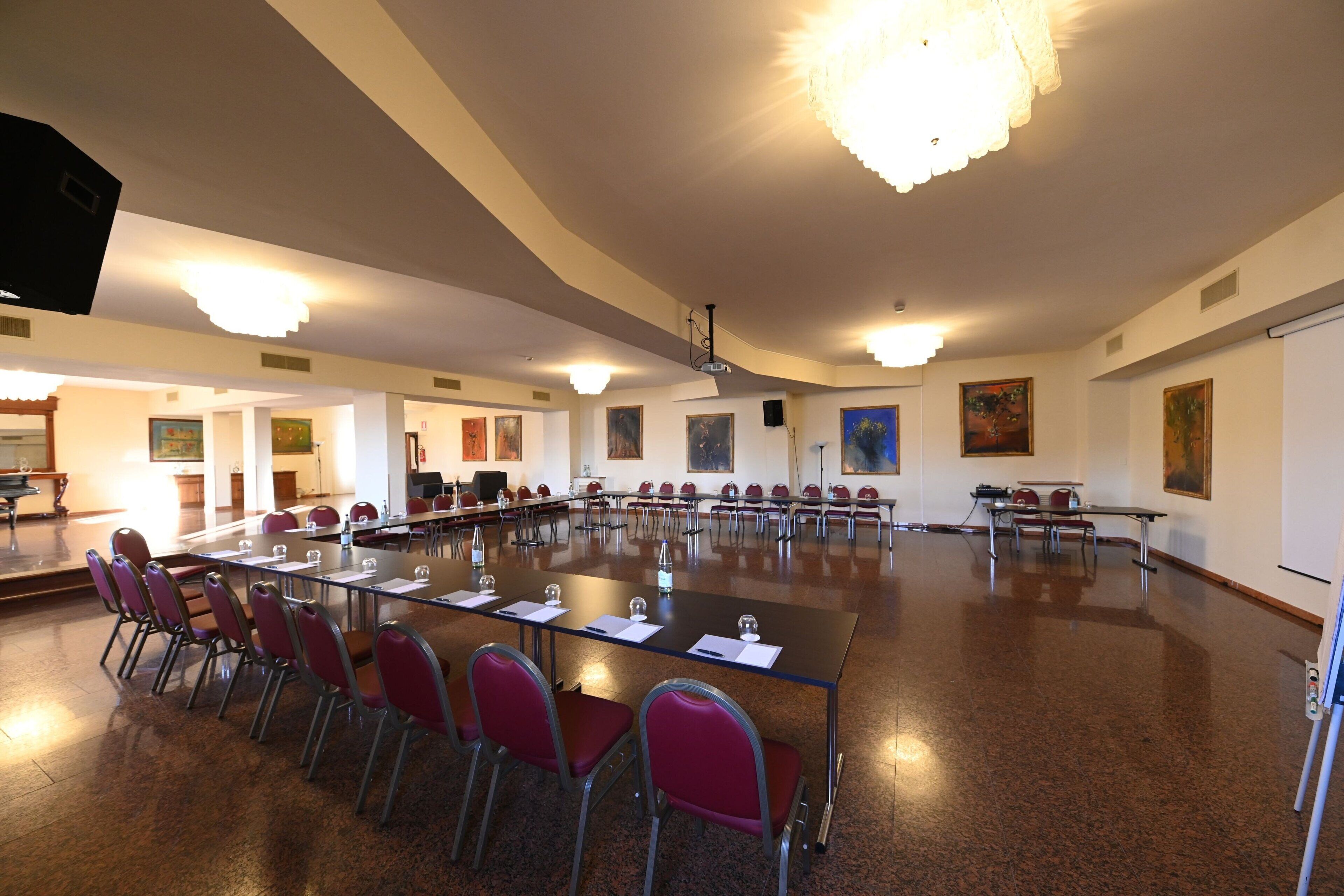 Un salón de conferencias con una larga mesa, sillas rojas y una pantalla de proyector.