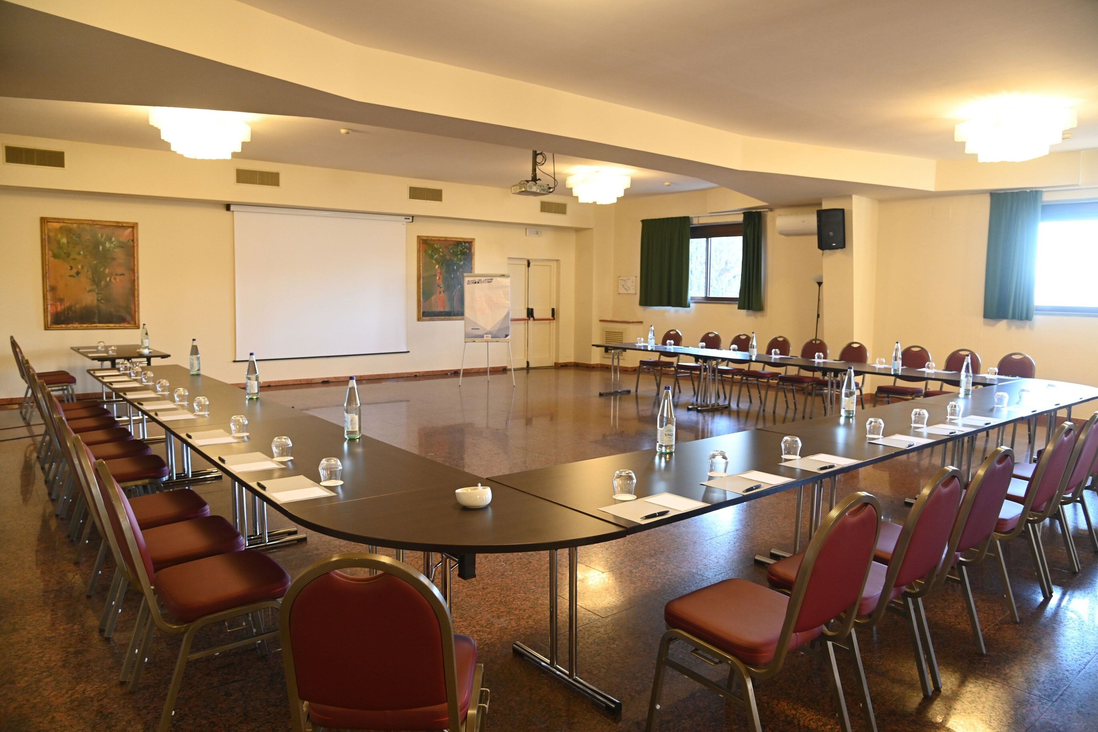 Una sala conferenze con un lungo tavolo, sedie rosse e uno schermo per proiezioni.