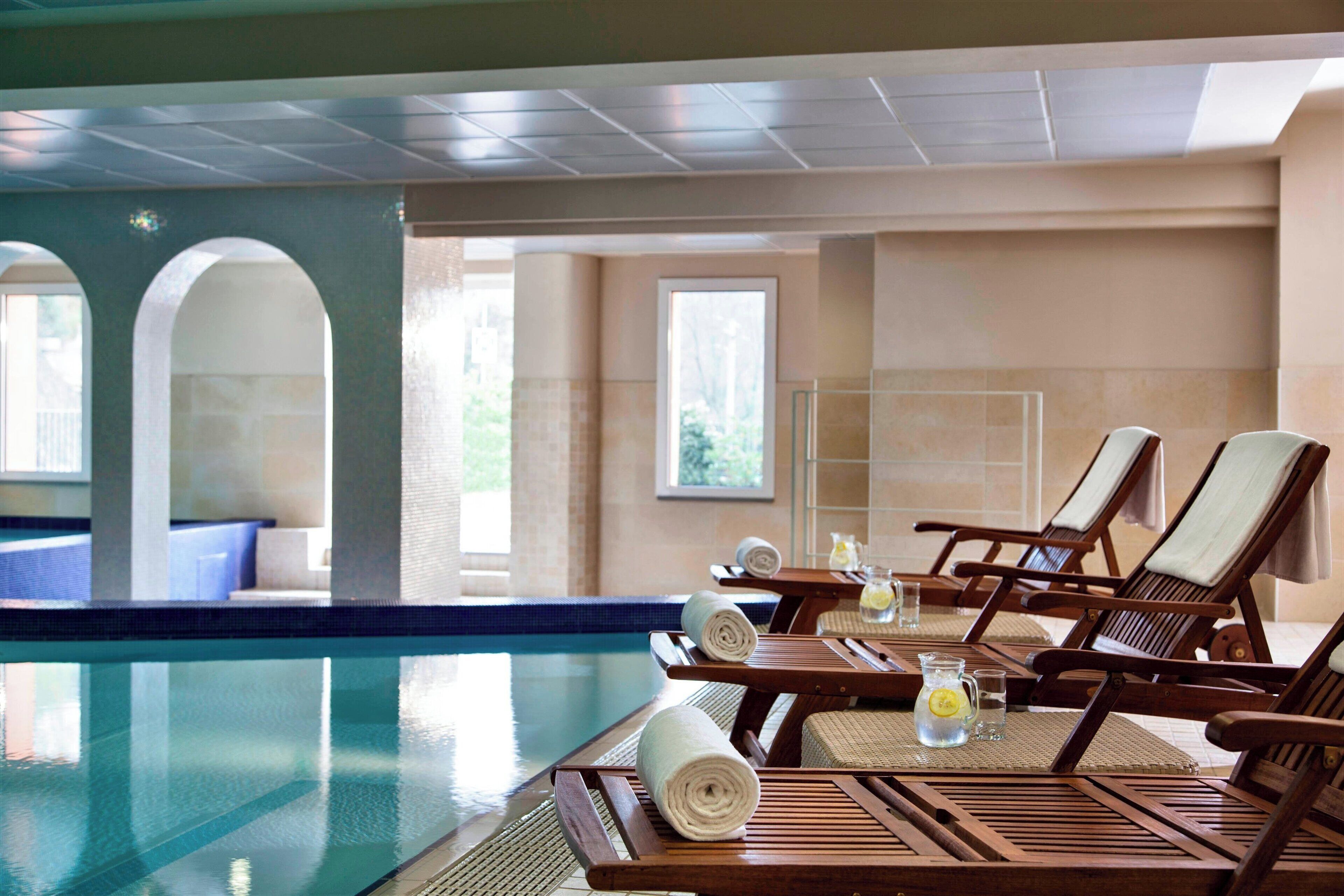 Zona junto a la piscina con sillones, una mesa con toallas y vista al agua.
