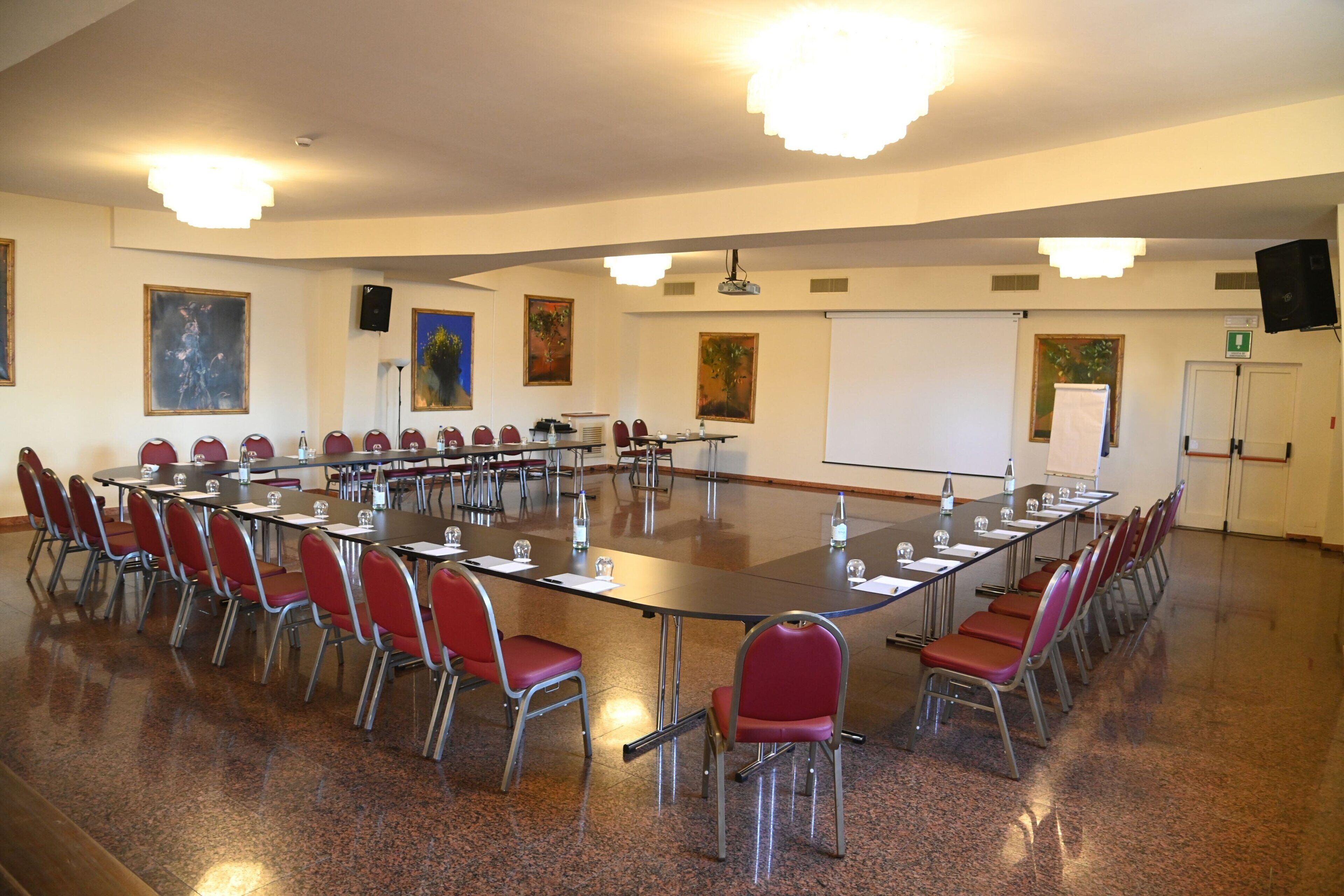 Une salle de conférence avec une longue table, des chaises rouges, un tableau blanc et des tableaux accrochés aux murs.