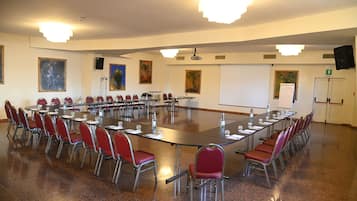 Une salle de conférence avec une longue table, des chaises rouges, un tableau blanc et des tableaux accrochés aux murs.