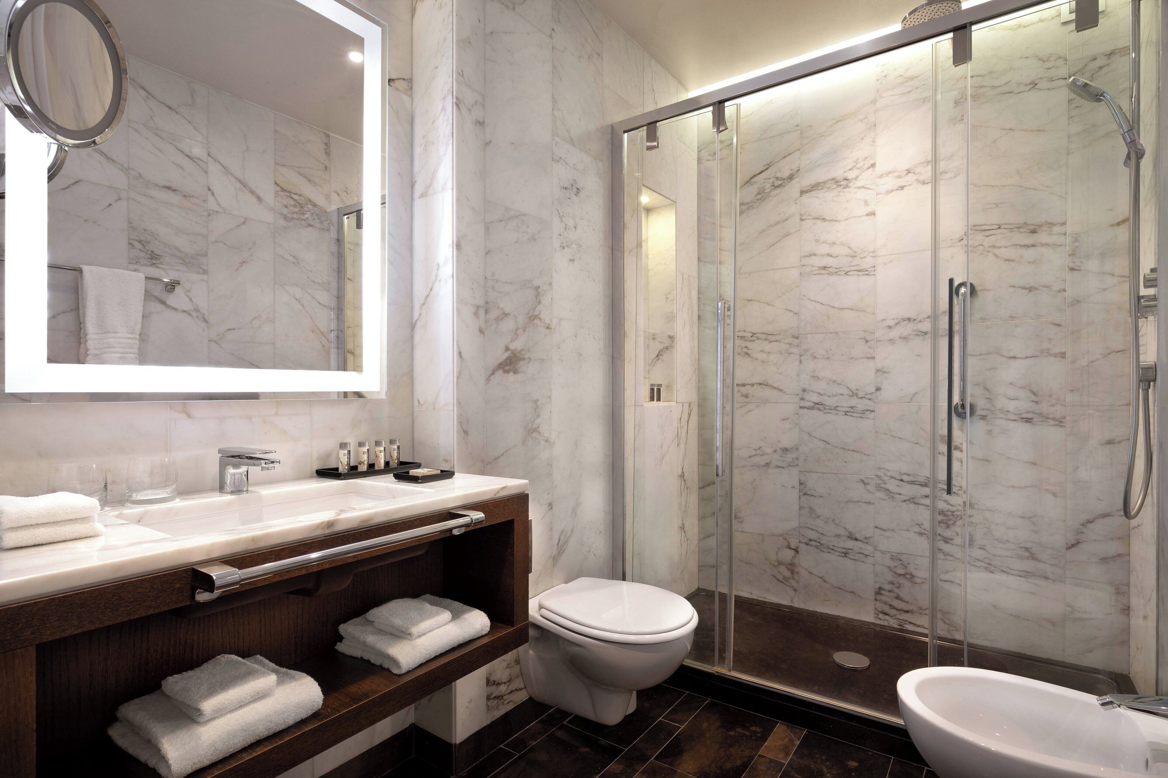 A modern bathroom with a marble vanity, a toilet, a glass-enclosed shower, and a large mirror.